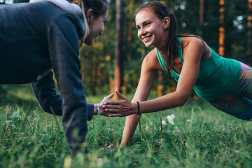 Two happy friends holding hands while doing plank exercise in park