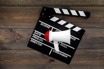 Naklejka premium Filmmaker concept. Electronic megaphone and clapperbord on dark wooden background top view copy space