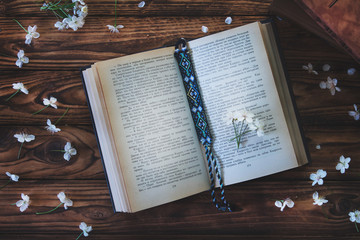 Fototapeta na wymiar open book with bookmark on wooden background and white spring flowers