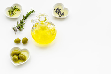 Fresh olive oil in glass jar near green olives and branch of rosemary on white background top view copy space