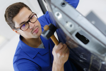 young handsome coachbuilder repairing broken car door