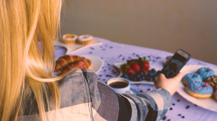 A girl or a woman takes a photo of food, breakfast, coffee, donuts, strawberries, coffee.
