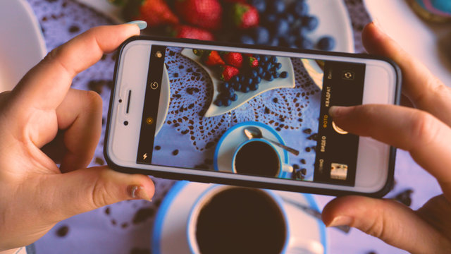 A girl or a woman takes a photo of food, breakfast, coffee, donuts, strawberries, coffee.