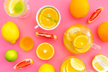 Refreshing summer tea with fruits. Teacup and teapot near orange, lime, lemon, grapefruit on pink background top view closeup