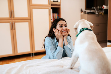 Brunette woman having fun with her dog in apartment.