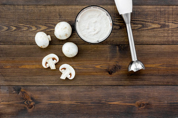 Cook cream soup with mushrooms. Champignon and blender on dark wooden background top view copy space