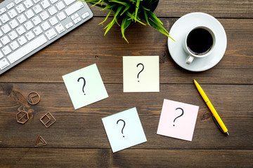 Question mark on sticky notes on office desk on dark wooden background top view. FAQ concept....