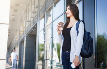 Young female asian IT student, with smartphone and backpack, drinking coffee before lesson and smiling