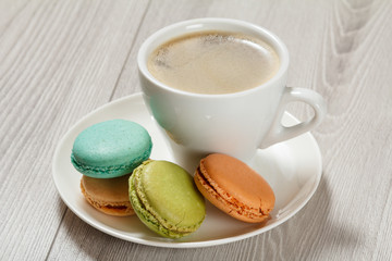 Cup of coffee, delicious macarons cakes of different color on white porcelain plate