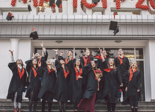Low angle view of happy students wearing graduation gowns standing on steps by building