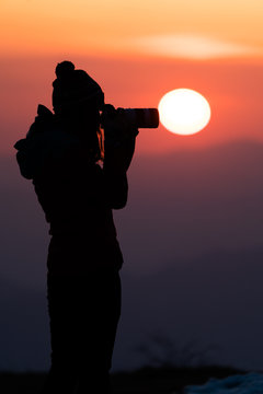 Young women photographer trying to capture the sunrise through her camera