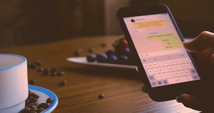 A girl or a woman, writes a message on the phone, a snack, a coffee mug on the table, coffee beans, strawberries and blueberries.