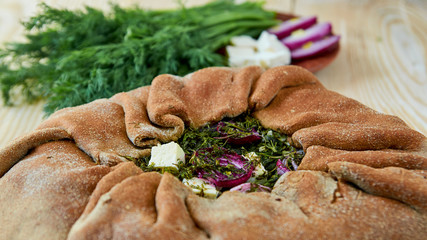 Pie with spinach, feta cheese, onion rings on the wooden table. Fresh baked whole pie decorated with fresh dill and other ingredients. Vegetarian pie close up view