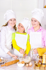 Cute little girls in chef's hats and aprons preparing dough in t