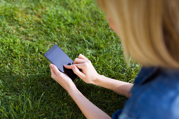 Pretty young woman using her mobile phone while lying on grass in the park.