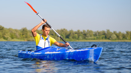 Young Professional Kayaker Paddling Kayak on River under Bright Morning Sun. Sport and Active Lifestyle Concept