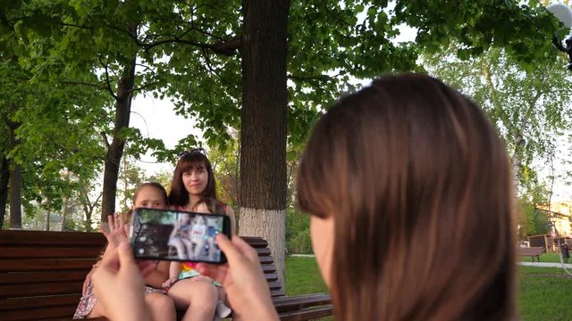 Young girl takes pictures of her mother, sister and small child on phone. Family selfies, on vacation in city.