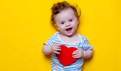 Fototapeten Little baby with heart shape toy on yellow background © Masson