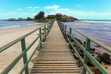Florianopolis, Santa Catarina, Brazil. Wooden pier on sandy beach with sea and island in background on sunny summer day.