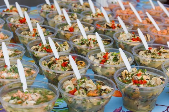 Display of different variety of ceviche in plastic glasses perfectly lined up with white spoons at Angelmo Bay market in Puerto Montt, Chile