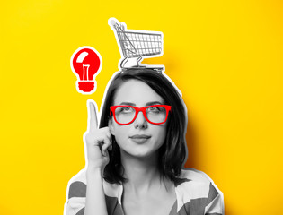 portrait of the beautiful young woman with cart for shopping and red idea bulb on the yellow...