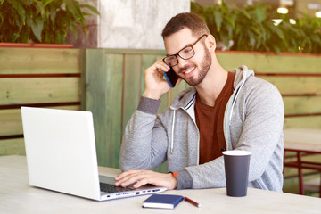 confident modern man in hoodie and t-shirt drinking coffee tea from a Cup sitting in a cafe with a laptop and talking