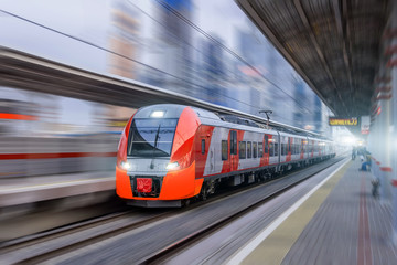 Fototapeta premium Szybki pociąg jedzie z dużą prędkością na stacji kolejowej w mieście.