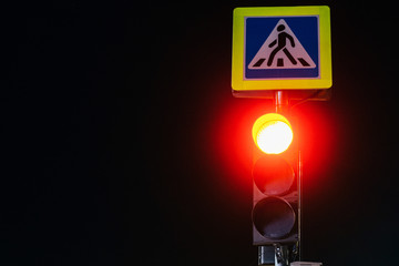 A traffic light at night shines with its lights and regulates a dangerous evening traffic.