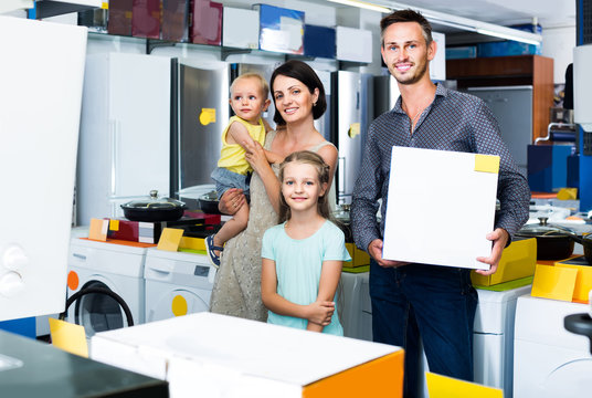 parents with two children shopping new electronics and holding box in shop of household appliances
