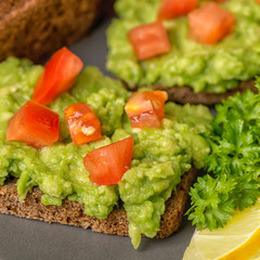 sandwiches with latin american mexican sauce guacamole with avocado, diced tomatoes and rye bread toast decorated sliced lemon, parsley on plate, detox concept