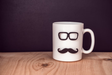 cup with mustache and glasses over chalkboard on wooden background, celebration concept of Fathers Day