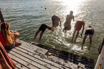 Children jumping from a pier in the sea.