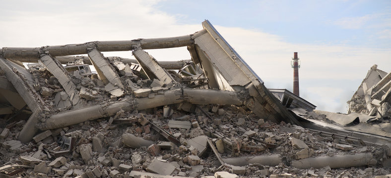 Industrial concrete building destructed by strike. Disaster scene full of debris, dust and crashed buildings