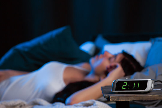 Photo of young woman with insomnia lying on bed next to clock