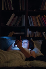 Photo of woman with phone lying in bed at night