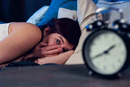 Portrait of brunette with insomnia lying on bed next to alarm clock at night