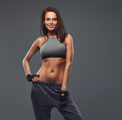 Smiling fitness brunette woman in a gray sportswear posing in a studio.