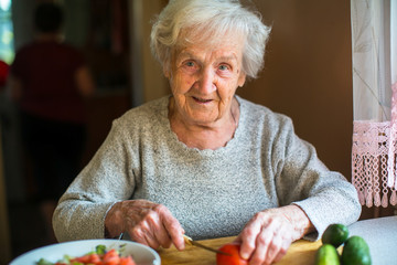 Elderly woman preparing vegetables for a salad.