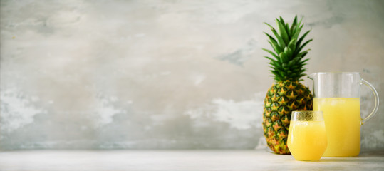 Pineapple juice in glassware and whole pineapple fruit on gray background. Copy space, sunlight...