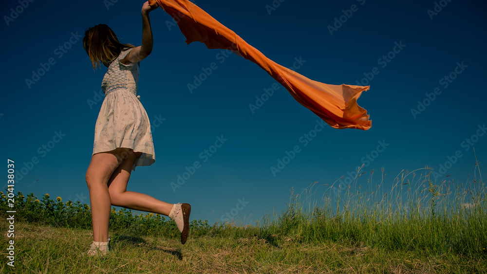 Sticker BEAUTIFUL BLONDE GIRL LAUGHS AND DANCES OUTDOORS WITH AN ORANGE SCARF IN HER HANDS