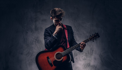 Obraz premium Handsome young thoughtful musician with stylish hair in elegant clothes posing with a guitar in his hands.