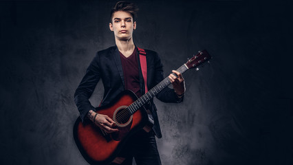 Obraz premium Stylish young musician with stylish hair in elegant clothes, playing on an acoustic guitar.