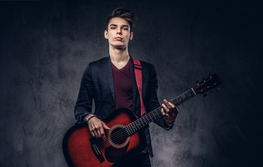 Stylish young musician with stylish hair in elegant clothes, playing on an acoustic guitar.