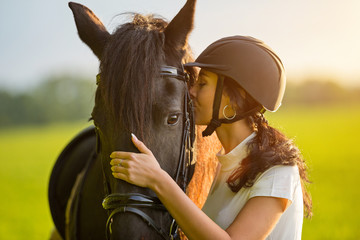 Young Woman kissing her horse at sunrise.