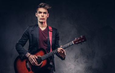 Stylish young musician with stylish hair in elegant clothes, playing on an acoustic guitar.