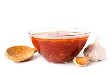 Plate of borscht with garlic and wooden spoon on a white background.