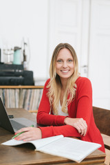 Cheerful blonde woman sitting in front ot laptop