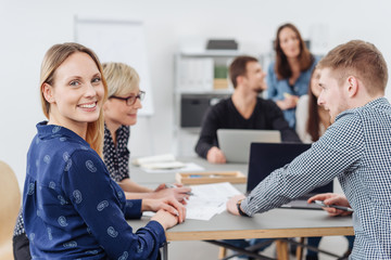 Smiling happy young woman in a busy office
