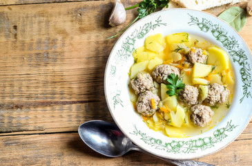 Meatball soup in a vintage plate and ingredients on wooden table. Top view.