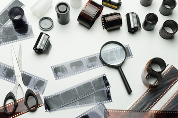 Different photographic films, scissors and magnifying glass on white background